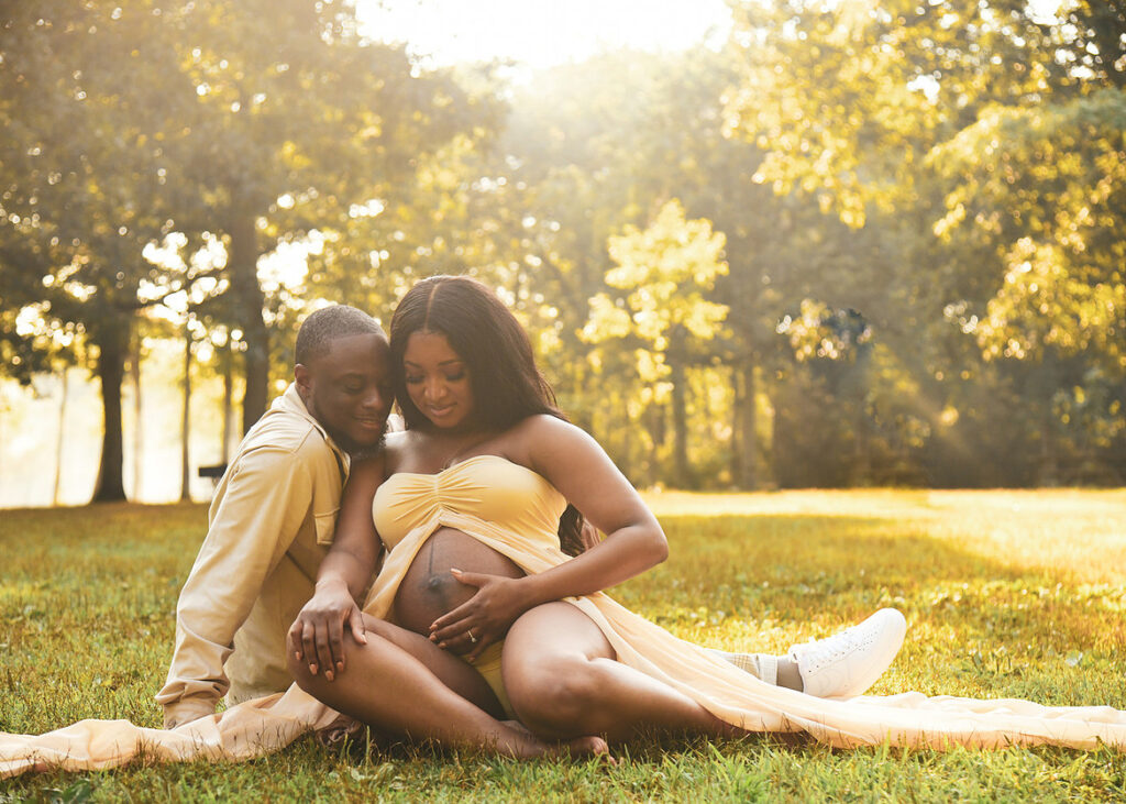 maternity photography couple seated on grass at golden hour sunset light