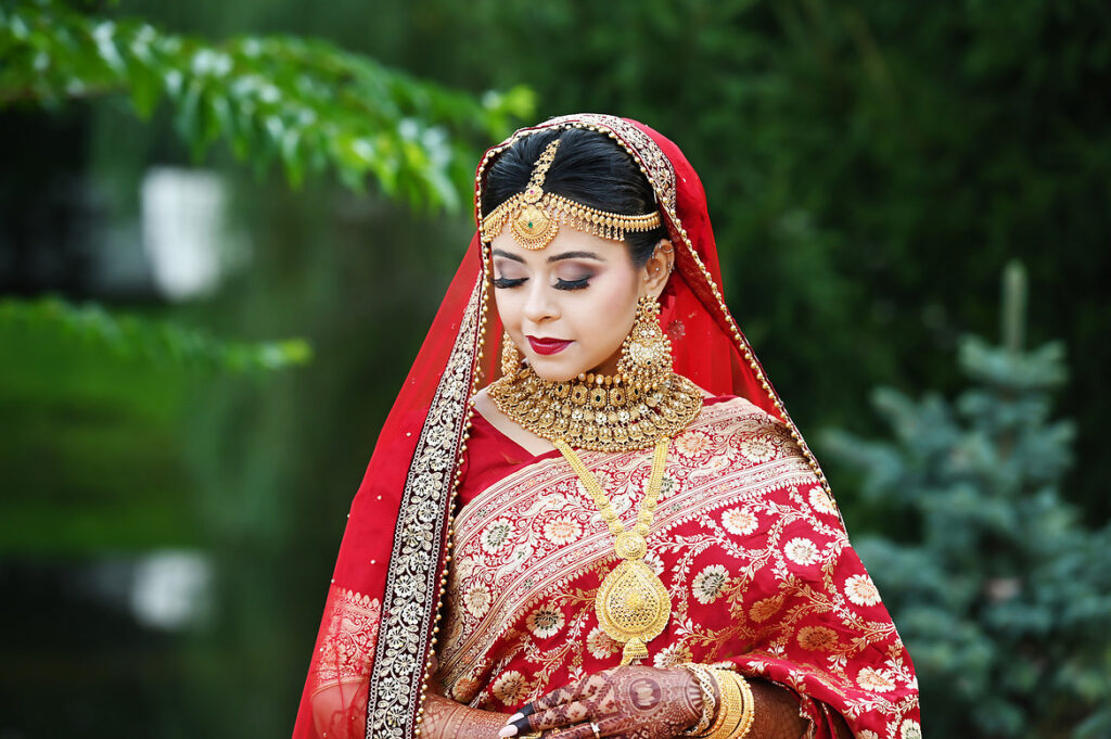 South Asian bride in red sari at Crest Hollow with detailed henna and jewelry.