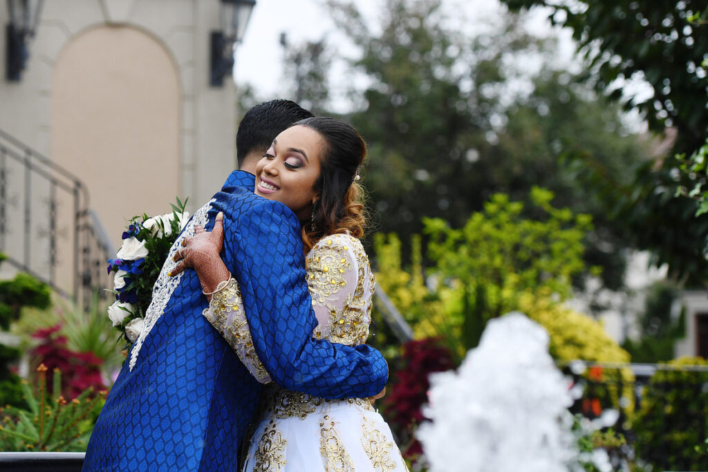 Bride and groom hugging outside Jericho Terrace in traditional wedding attire, candid and natural moment.