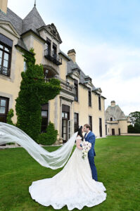 Bride and groom kissing at Oheka Castle as the veil blows in the wind during wedding portraits
