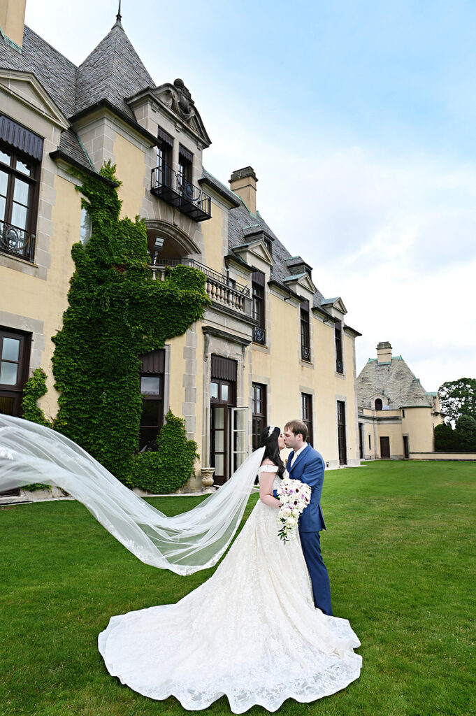 Bride and groom kissing at Oheka Castle as the veil blows in the wind during wedding portraits
