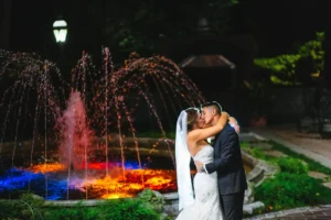 Bride and groom posing at night in front of the illuminated fountain at Westbury Manor, captured in a romantic wedding portrait.