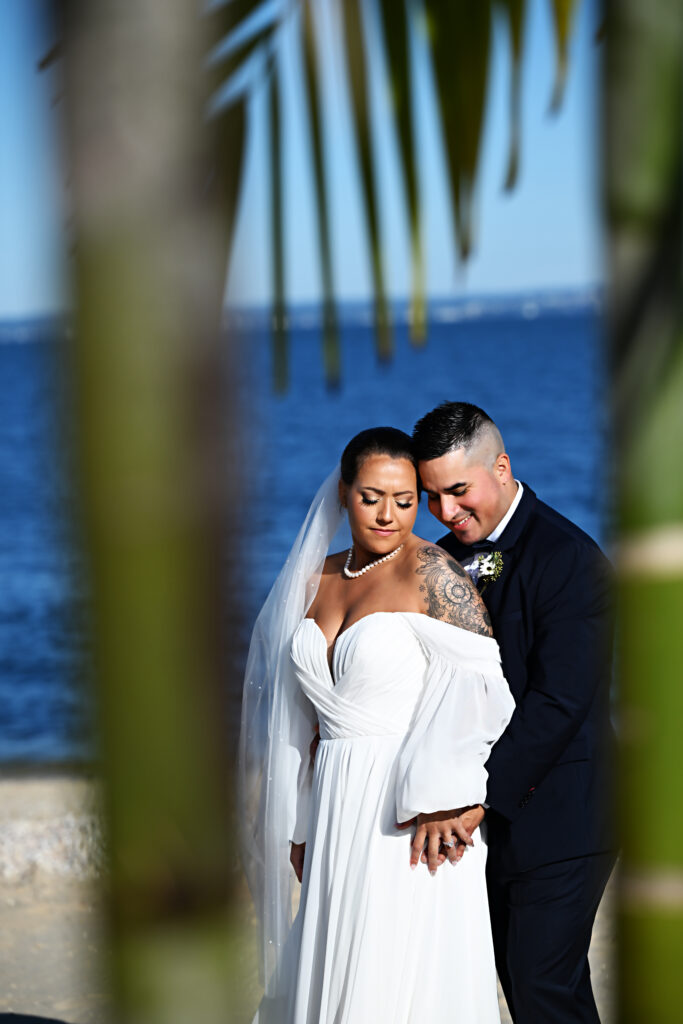Bride and groom portrait framed by palm leaves with ocean backdrop at Crescent Beach Club Long Island New York