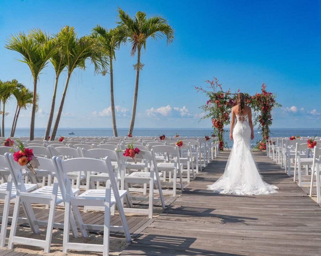 Beach ceremony setup with chairs, floral arch, palm trees and ocean at Crescent Beach Club Long Island New York