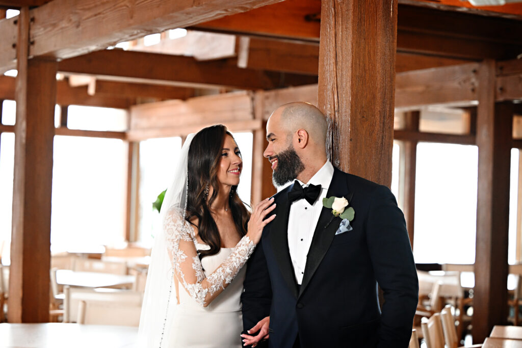 Bride and groom facing each other for romantic portrait under wooden beams at Crescent Beach Club Long Island New York