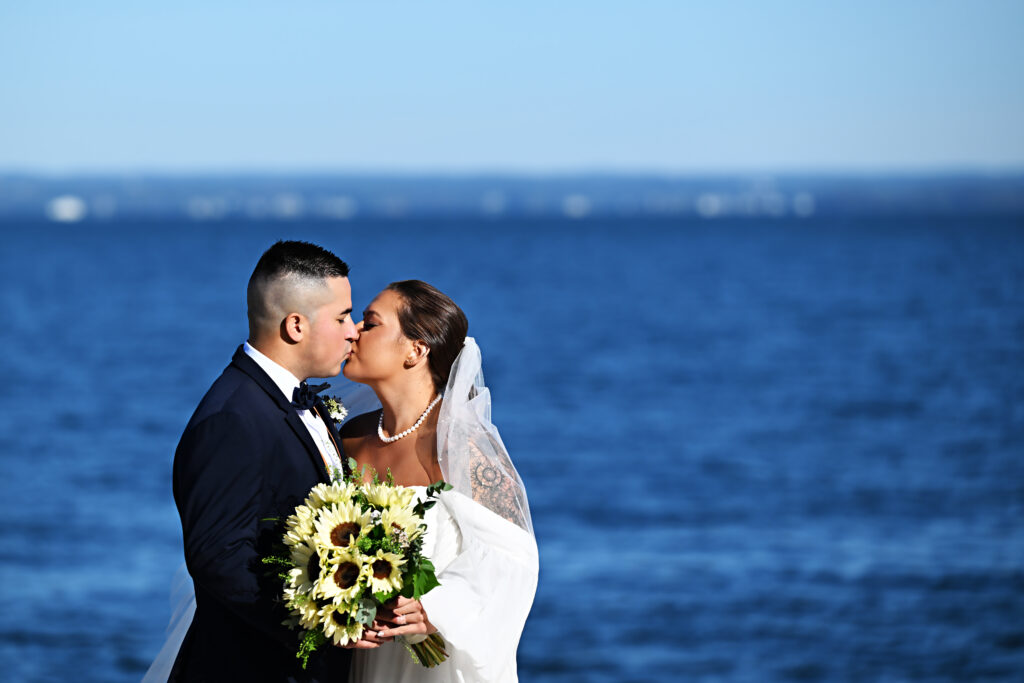 Bride and groom kissing with bouquet by the ocean at Crescent Beach Club Long Island New York
