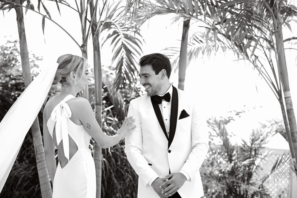 Black and white candid wedding portrait of bride and groom under palm trees at Crescent Beach Club, Long Island, New York.