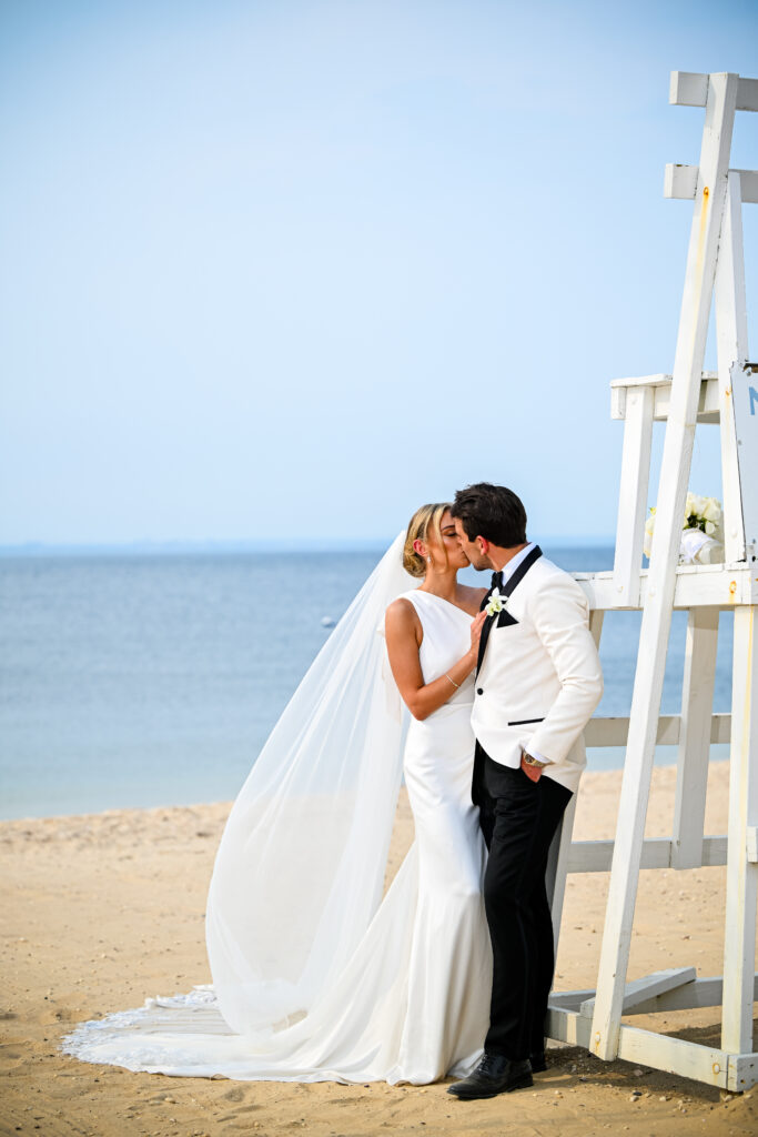 Bride and groom kiss near lifeguard stand on Crescent Beach Club beach, Long Island, New York.