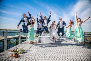 Bridal party jumping together on a waterfront dock during a joyful wedding celebration photographed by Patken Photographer