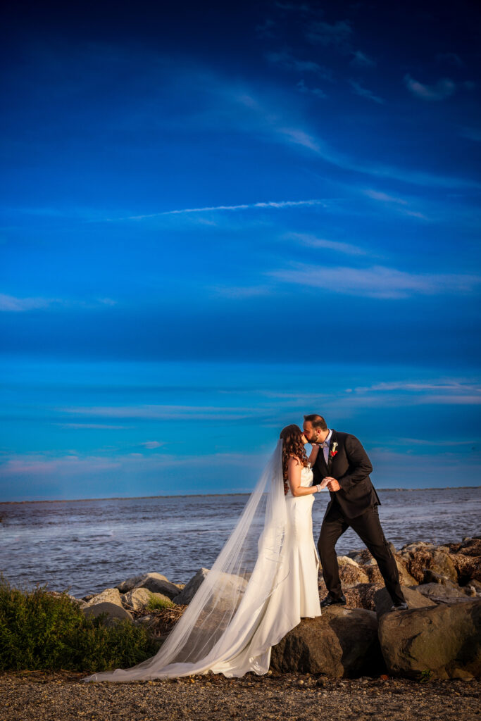 Bride and groom standing together on the beach at Land’s End during their wedding, captured in natural coastal light.