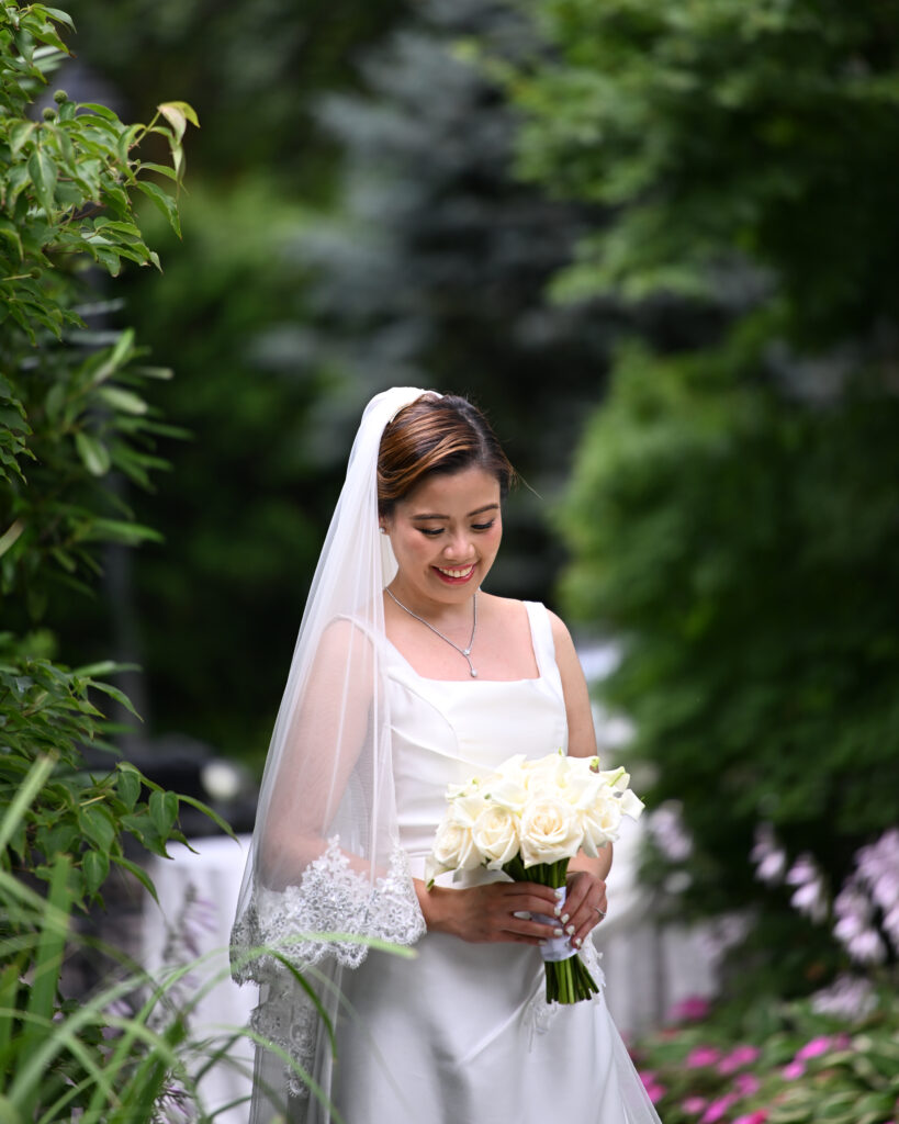 Bride holding bouquet in lush garden during Long Island wedding