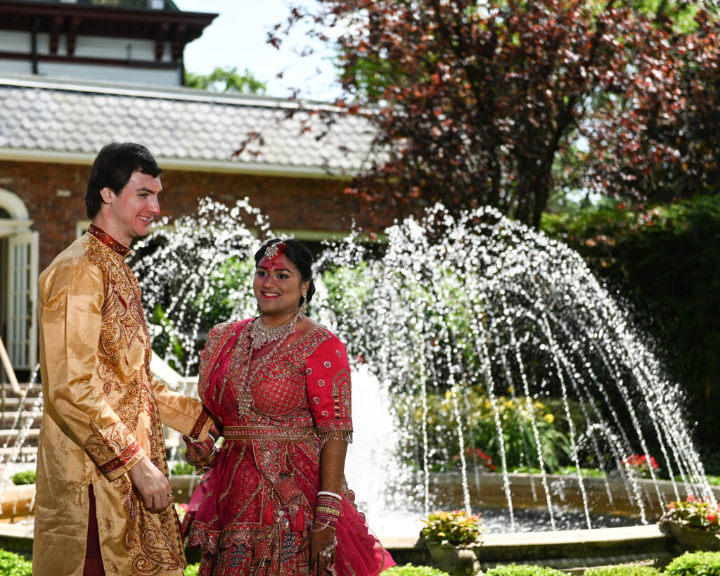 South Asian bride and groom in traditional attire at Westbury Manor fountain Long Island