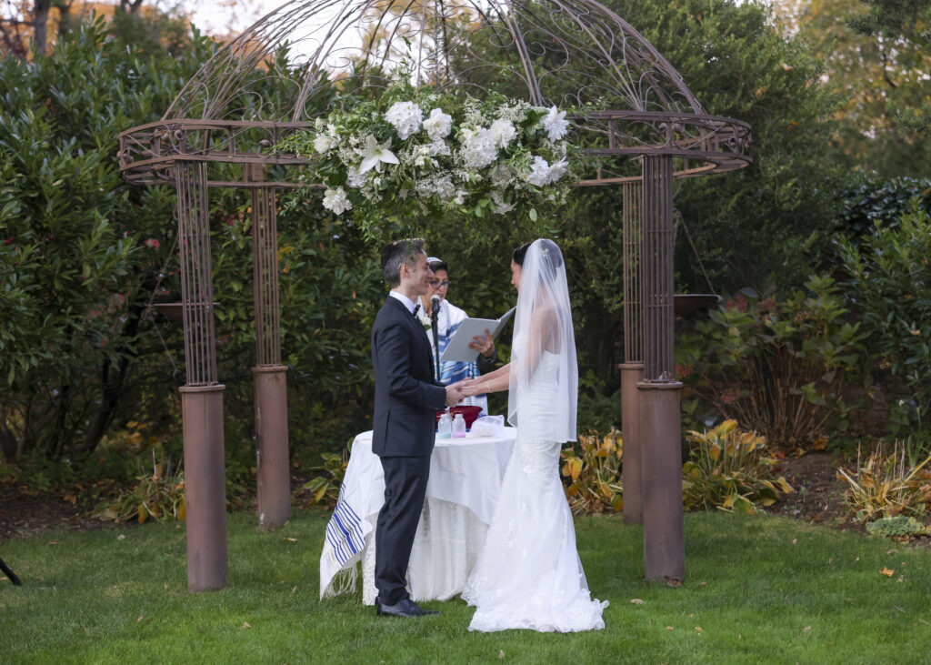 Bride and groom exchanging vows under garden pergola at Westbury Manor Long Island