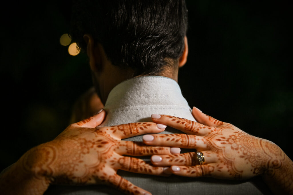 Bride hands with henna resting on groom’s shoulder at Westbury Manor