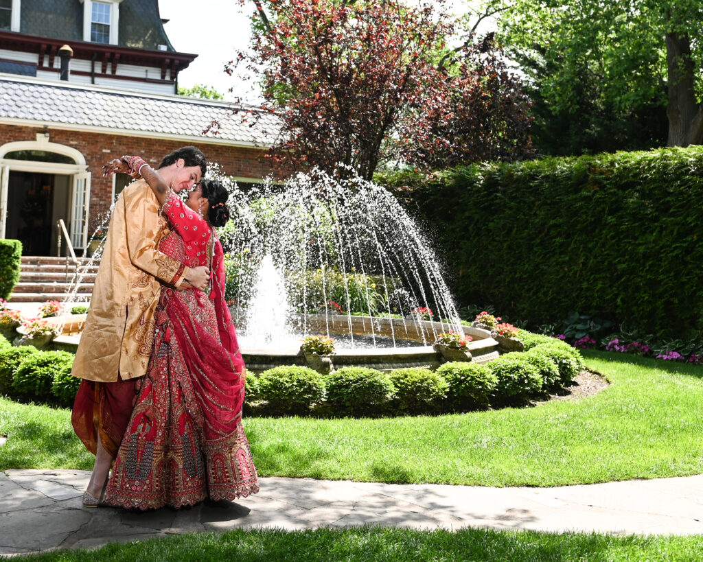 South Asian bride and groom posing near fountain at Westbury Manor Long Island